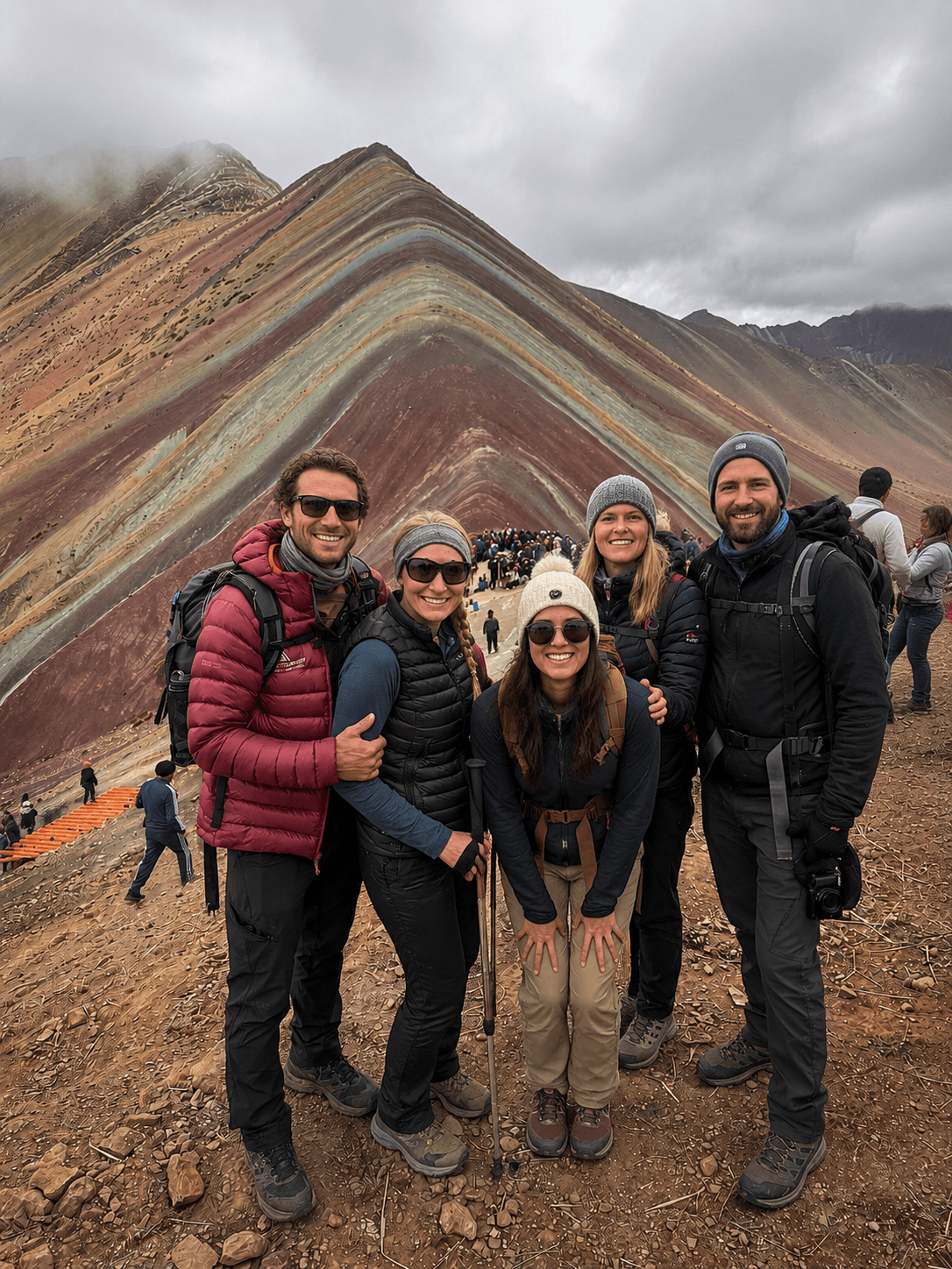 Five travelers posing in front of the colorful slopes of Vinicunca in the Peruvian Andes.