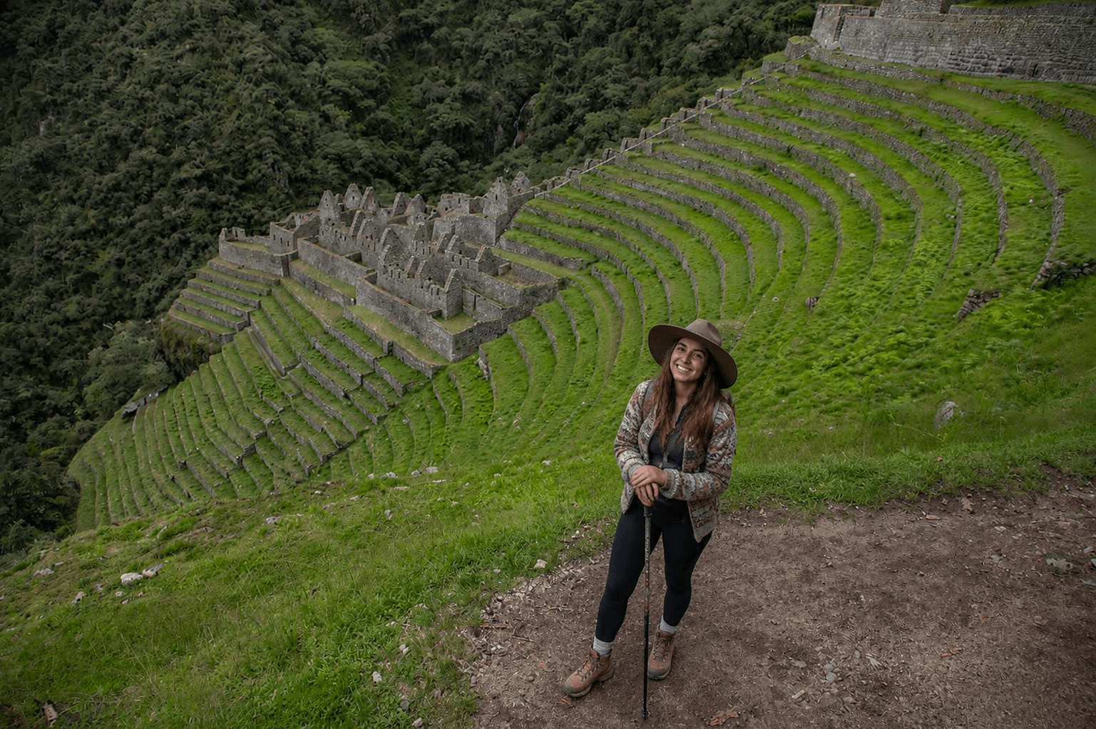 Traveler walking through the Inca terraces and paths of Wiñay Wayna, surrounded by green mountains and cloud forest vegetation.